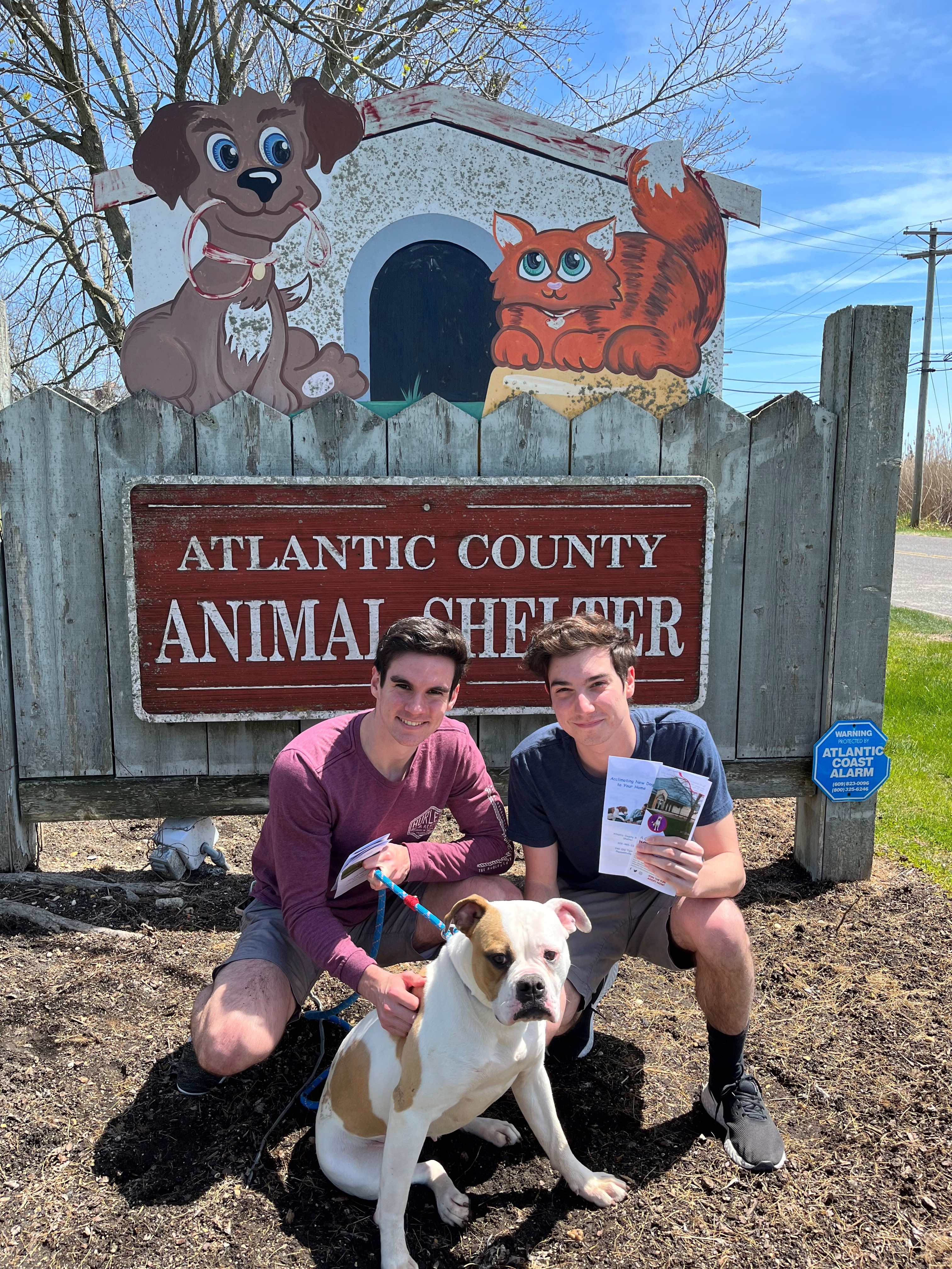 Two young men holding the pamphlets in front of the Animal Shelter Sign with a dog on a leash.