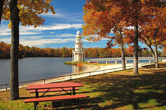  Lighthouse with lake and red picnic table in foreground.